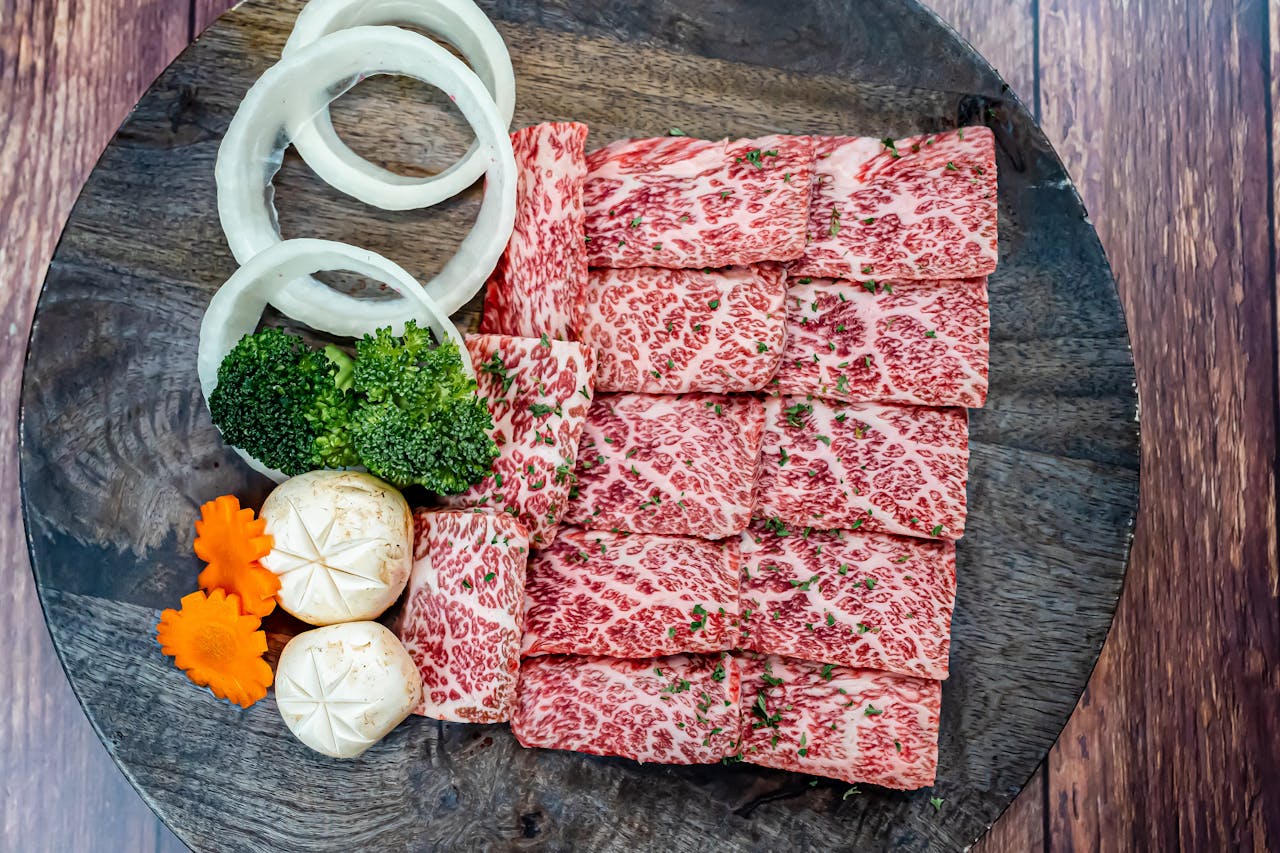 Sliced raw Wagyu beef with vegetables artfully arranged on a wooden platter for a gourmet dining experience.