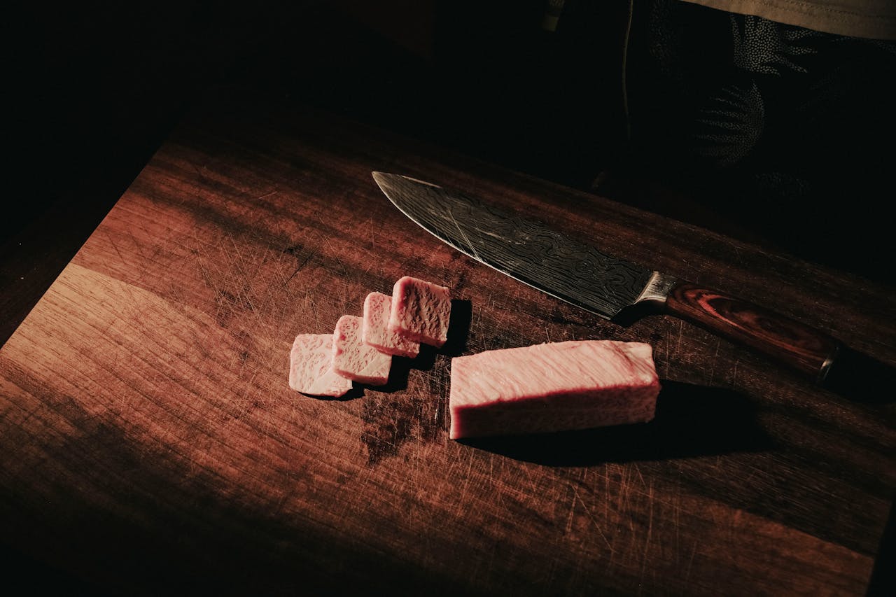 Sliced wagyu beef with exquisite marbling on a wooden board, accompanied by a chef's knife.