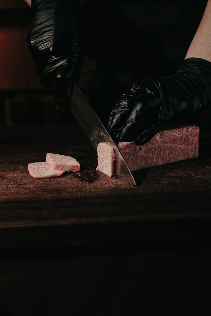 Close-up of hands slicing marbled Wagyu beef on a wooden surface, emphasizing texture and craft.