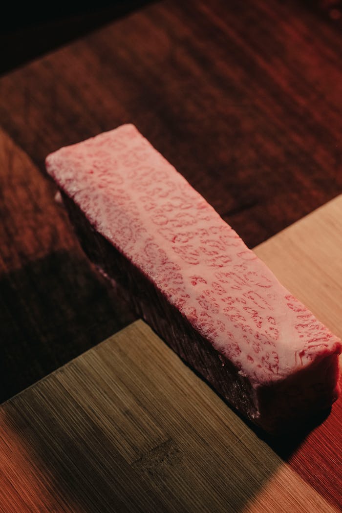 Close-up of raw marbled Wagyu beef steak on a wooden cutting board, showing intricate fat marbling.