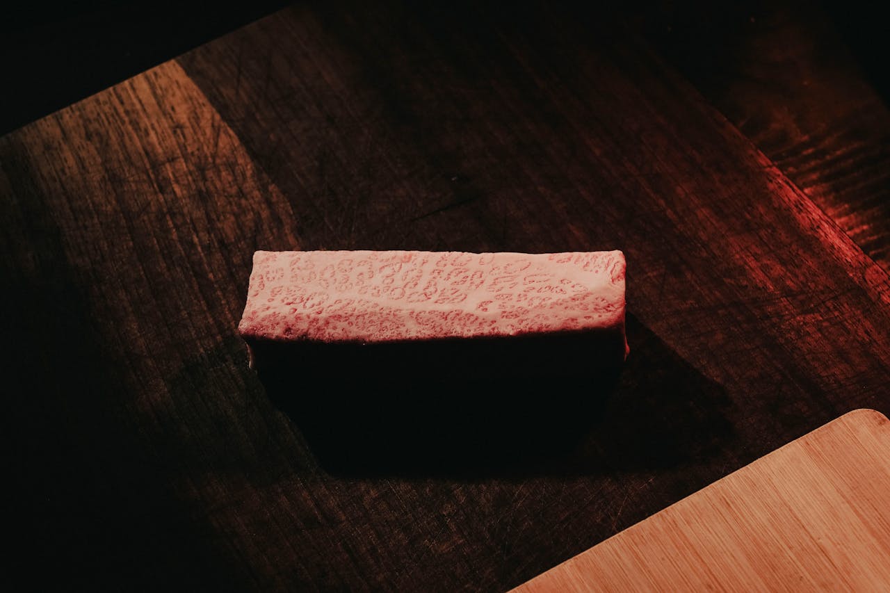 Close-up of marbled Wagyu beef on a rustic dark wooden table, showcasing rich texture and color contrast.